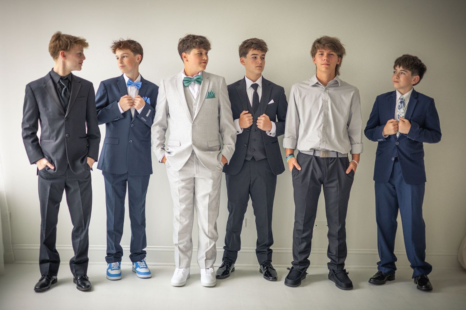 Six teenage boys in formal suits pose together, adjusting their jackets for a prom or formal event photo.
