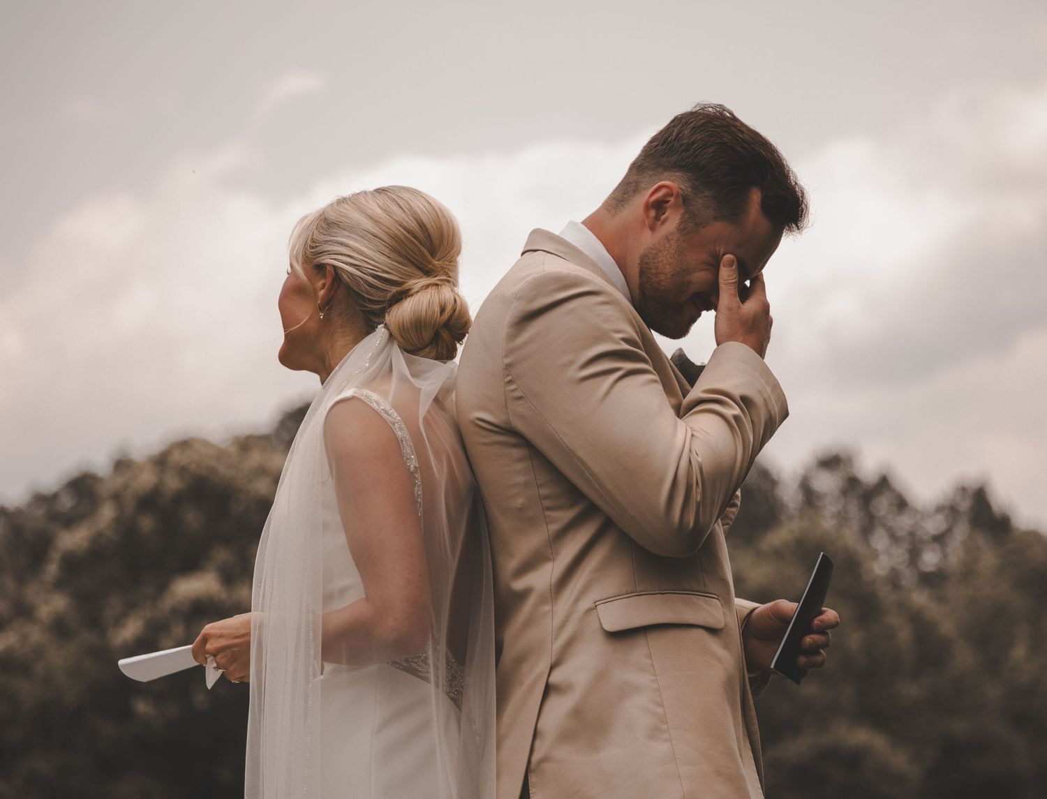 Emotional first look moment between couple against cloudy sky backdrop.