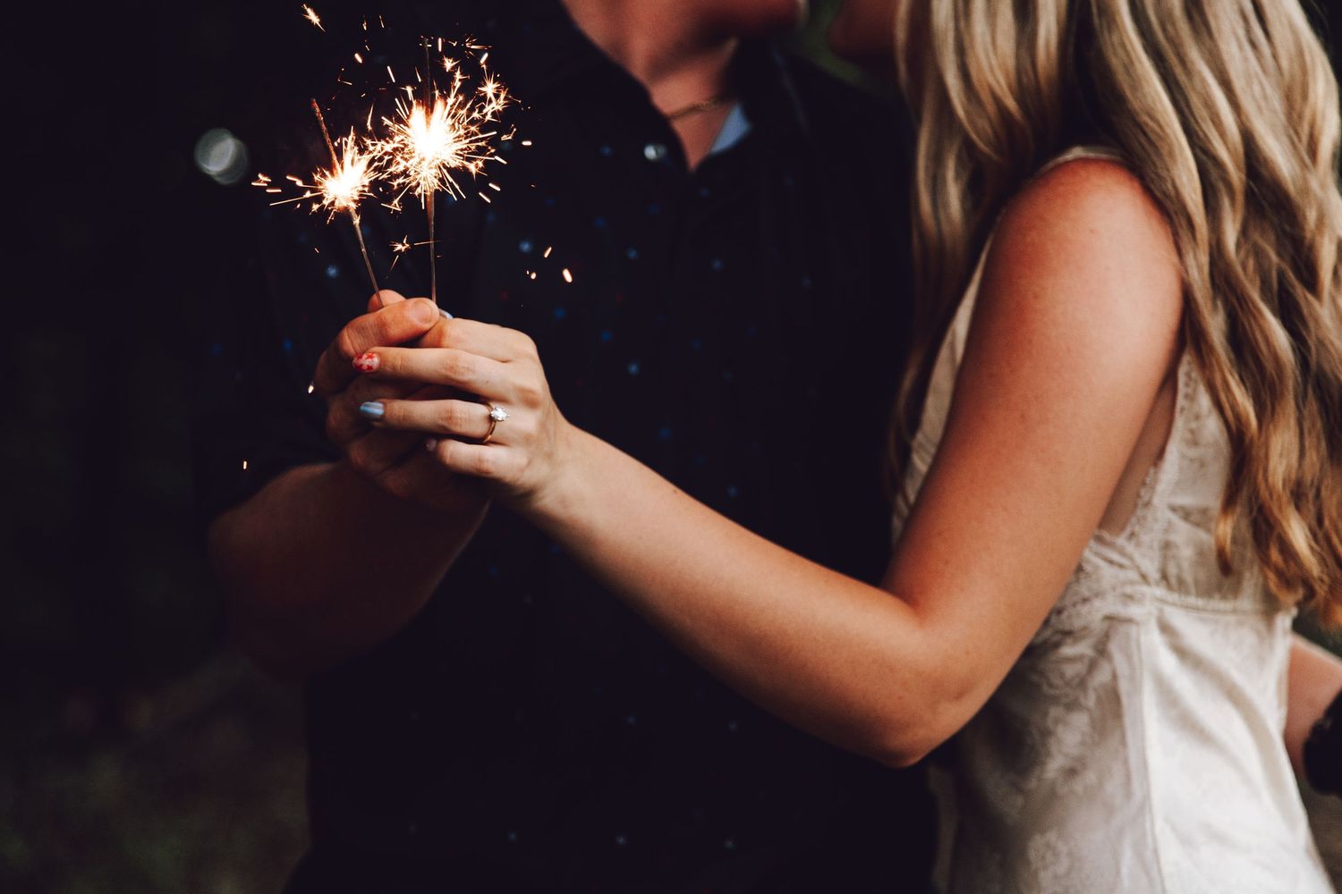 Two people share an intimate moment while holding sparklers in the dark.