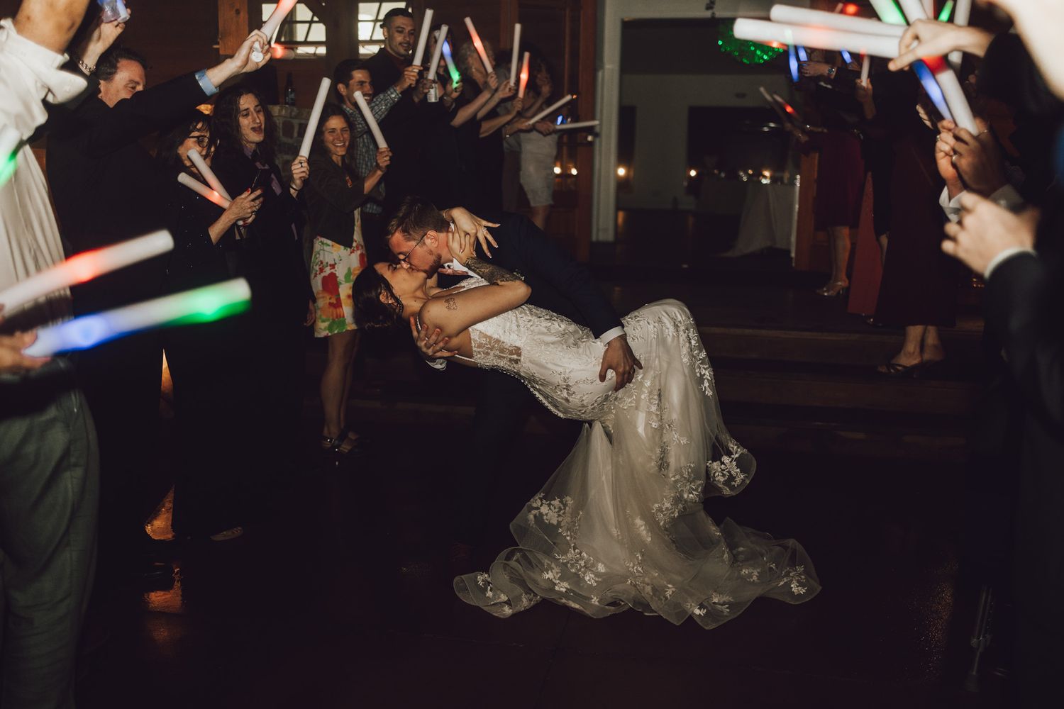 Wedding celebration in dark venue with guests waving colorful LED light sticks.