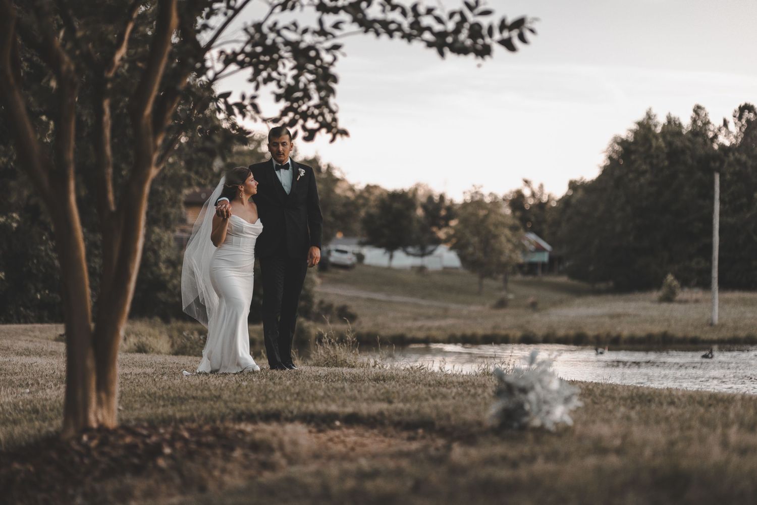 A tranquil wedding portrait by a pond with trees framing the romantic scene.