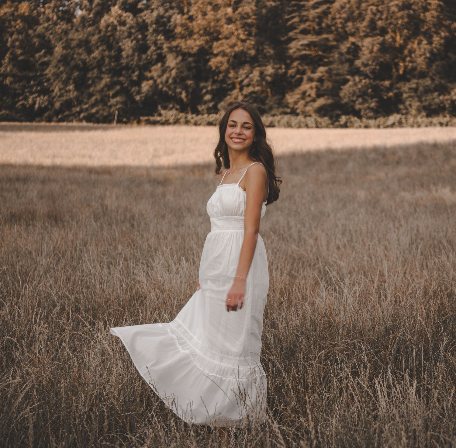 White sundress flowing in a golden field during sunset with dramatic lighting and natural backdrop.
