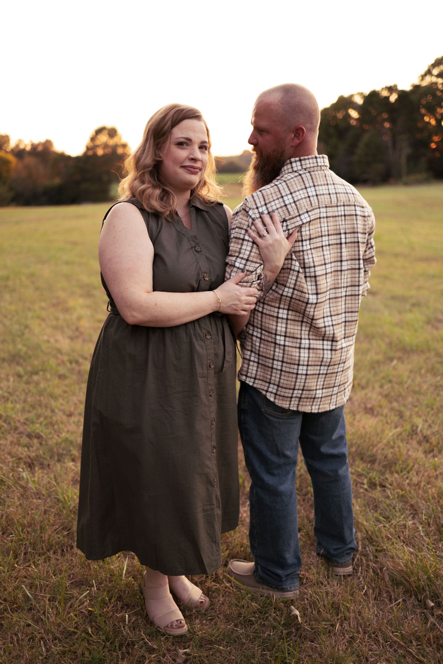 A couple shares a tender moment in a field at sunset wearing casual attire.