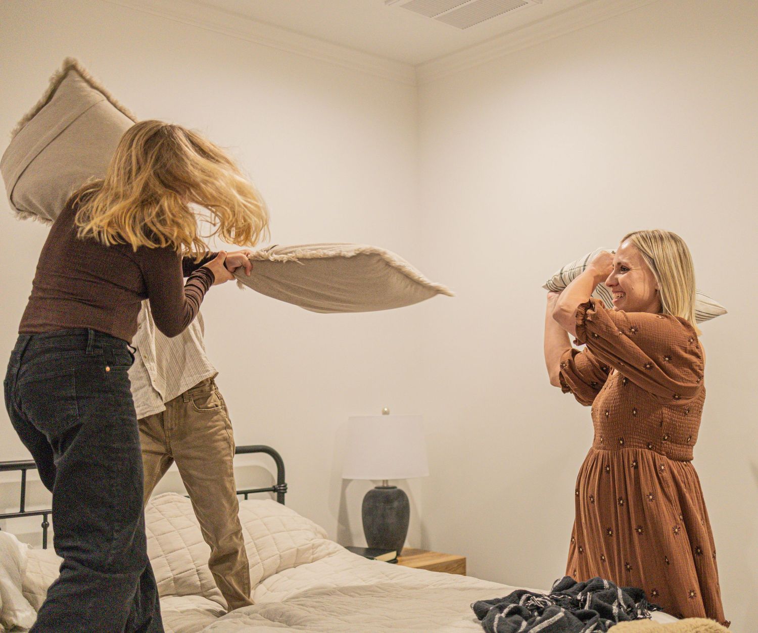 Two people engaged in an energetic pillow fight on a bed in a minimalist room.