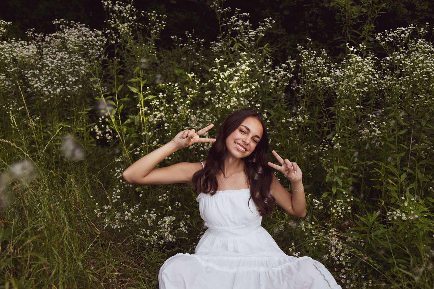 Playful summer pose in a white dress surrounded by wild meadow flowers.