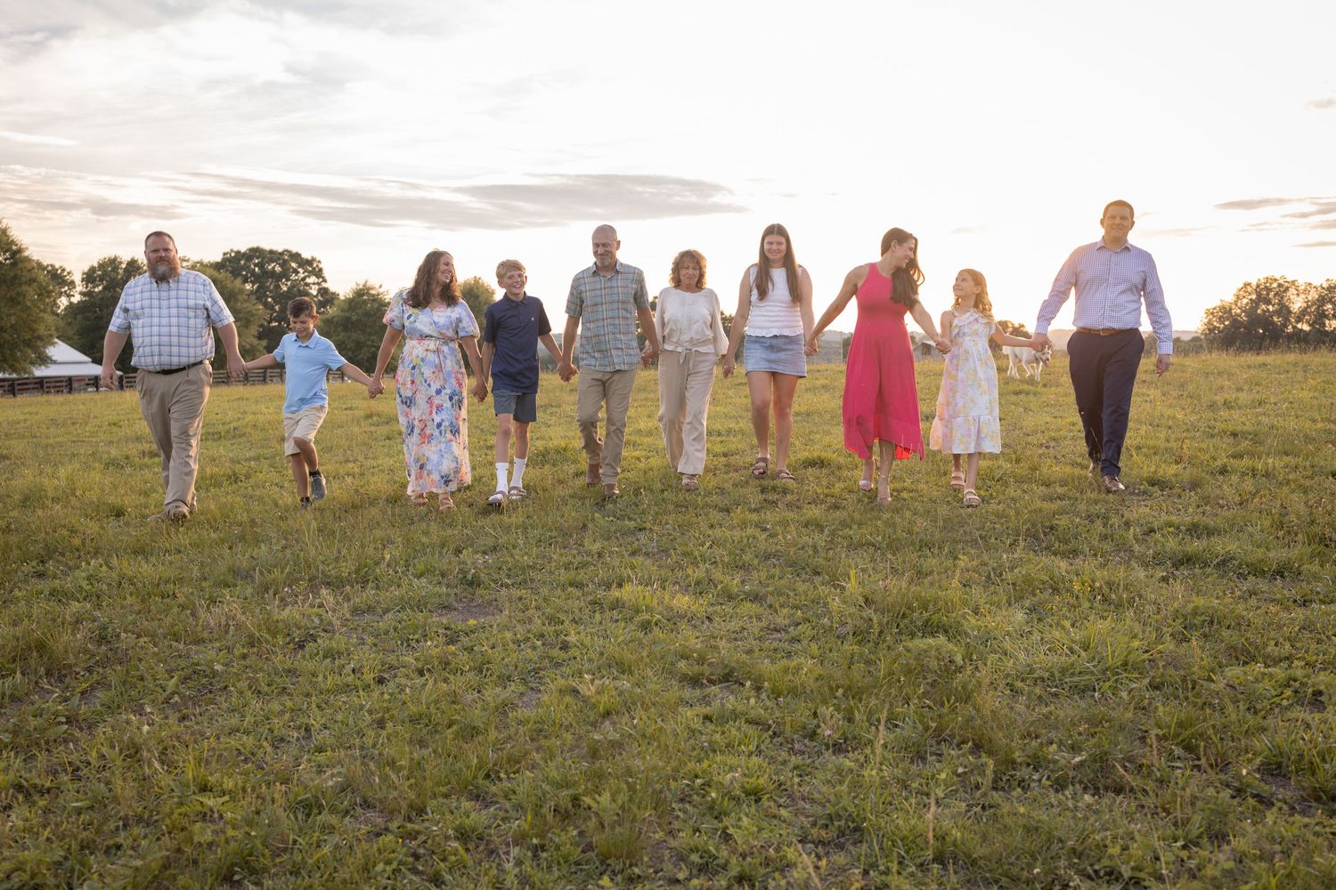 Large family holding hands walking through a green field at sunset in matching outfits for a portrait.