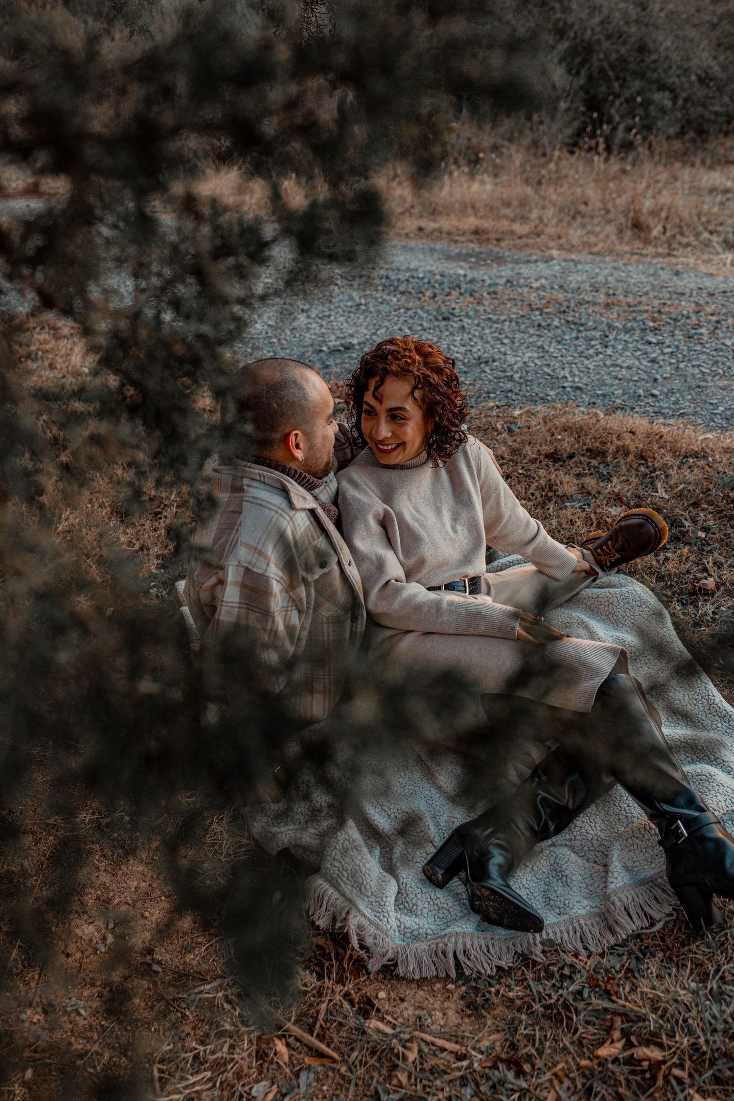 Intimate couple moment captured through foliage in warm moody lighting.