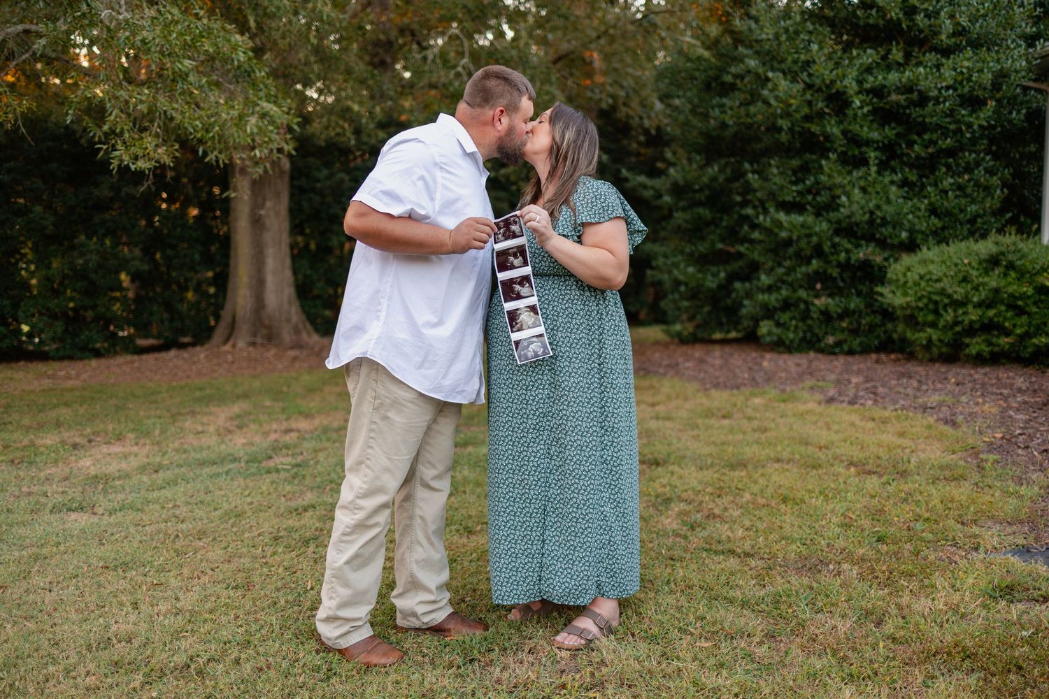 A romantic outdoor proposal scene unfolds in a grassy park setting with trees in the background.