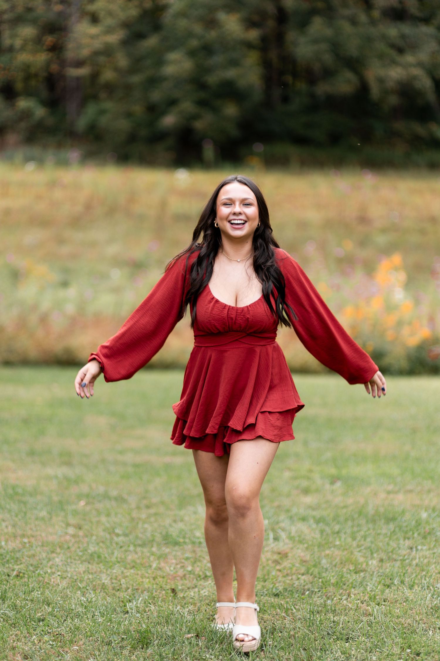 A person in a flowing red dress twirls playfully in a grassy field on a sunny day.