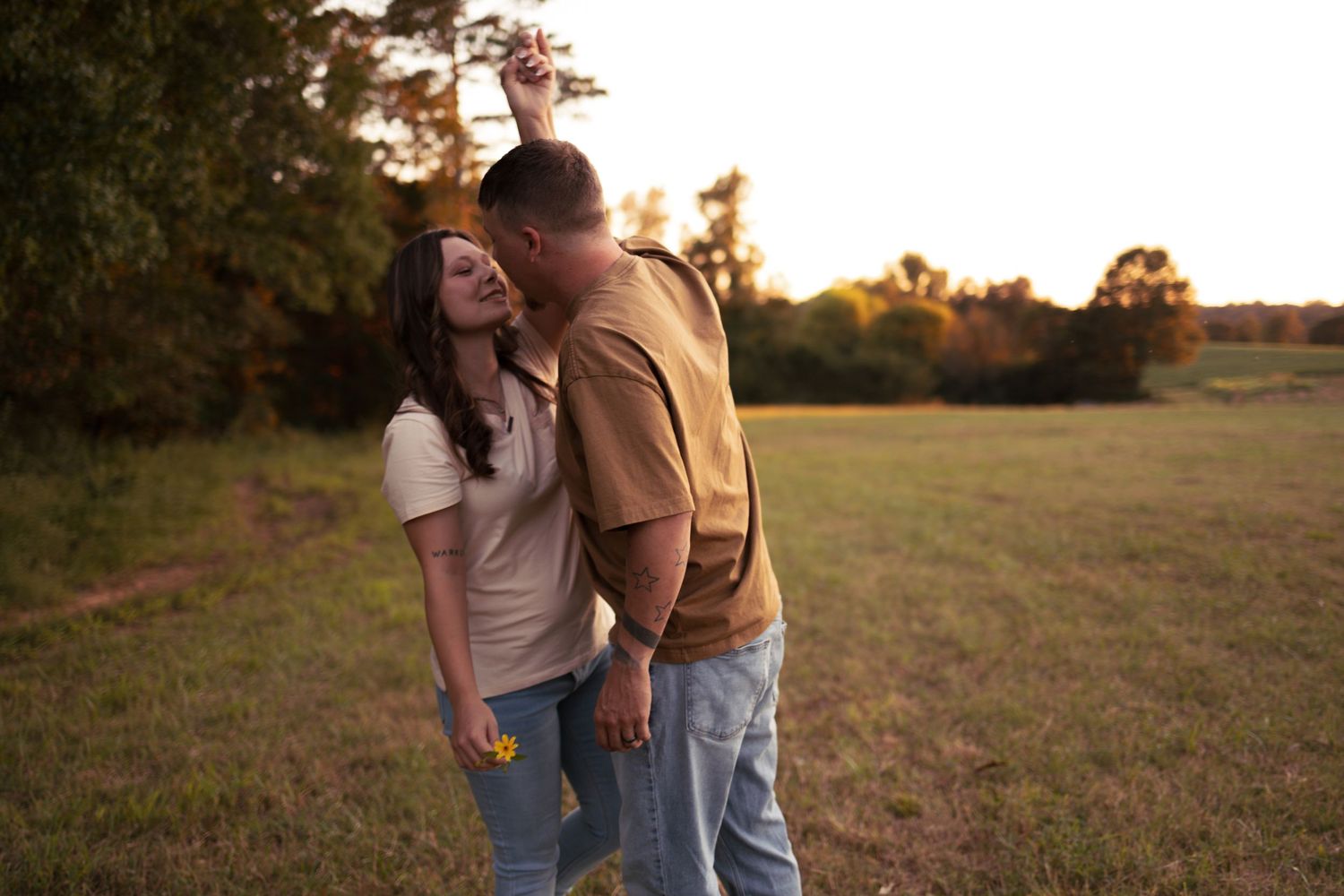 A couple embraces while standing in a golden field at sunset, creating a romantic silhouette against the warm sky.