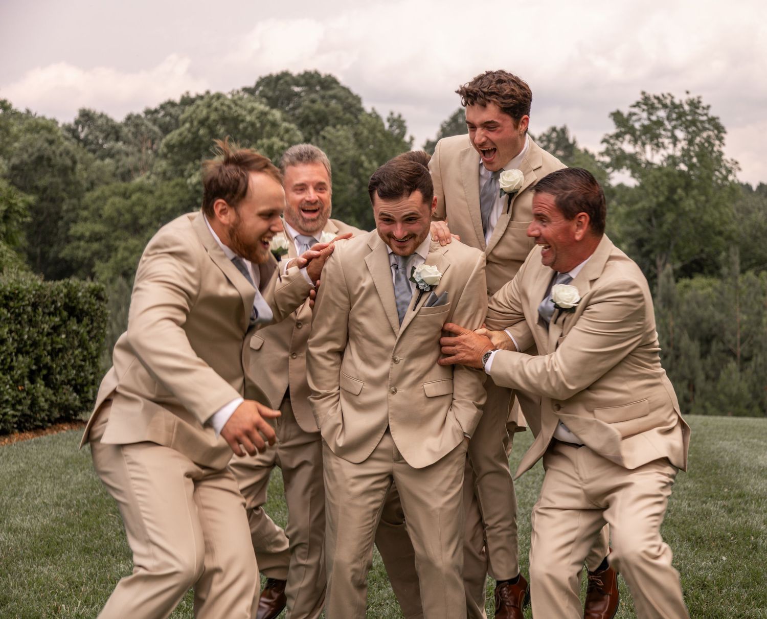 Wedding party in tan suits celebrating with energetic group poses outdoors.