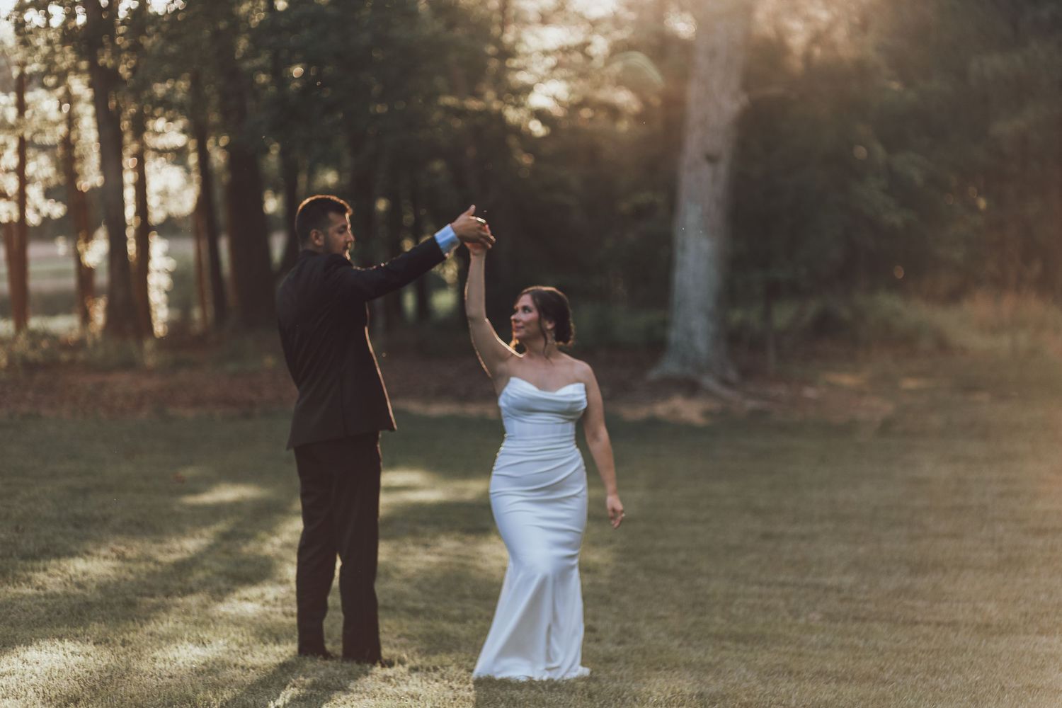 A couple dances joyfully on their wedding day in a sunlit forest clearing.