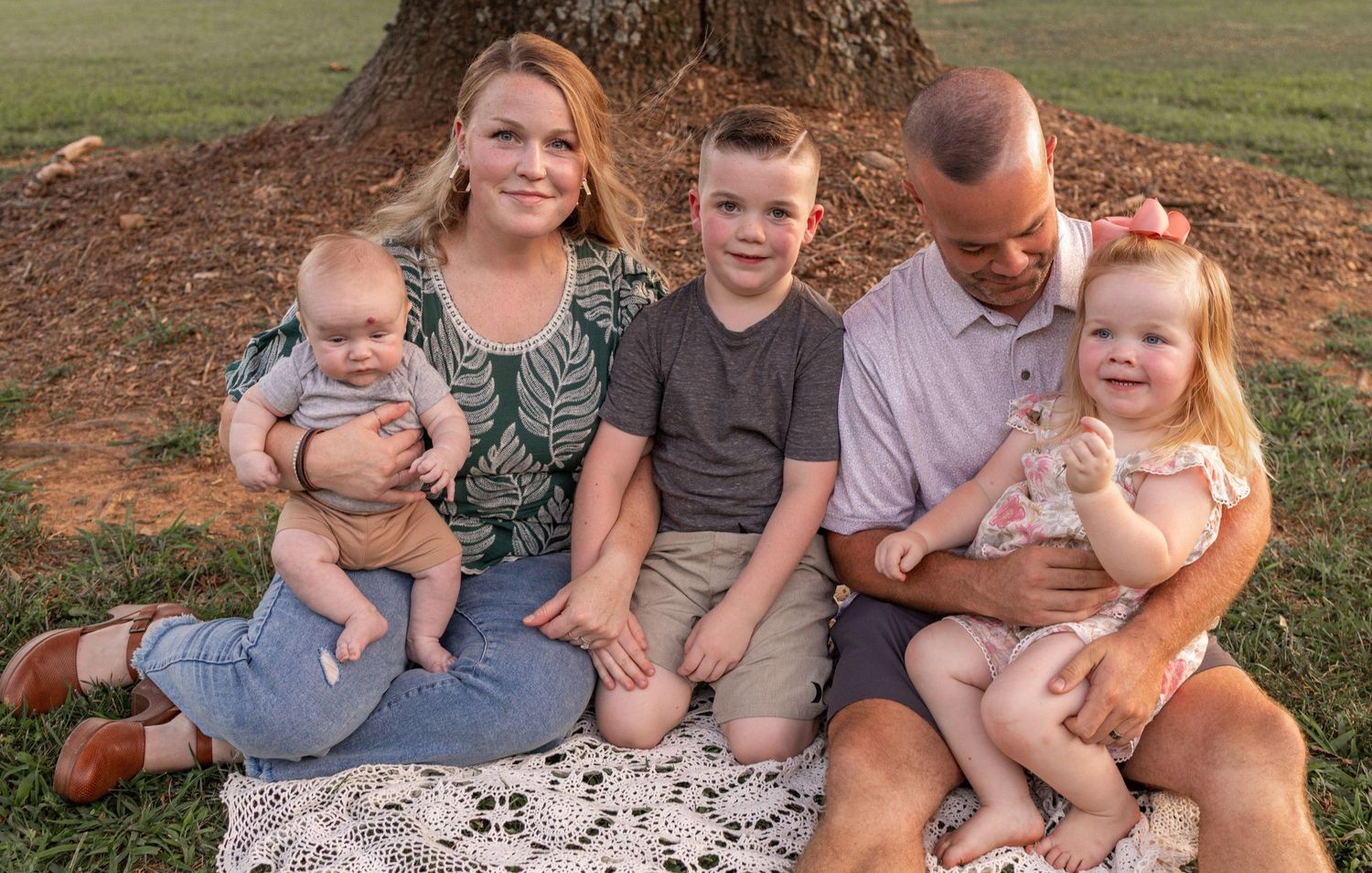 Group sitting together on grass lawn during golden hour outdoor family photoshoot session.