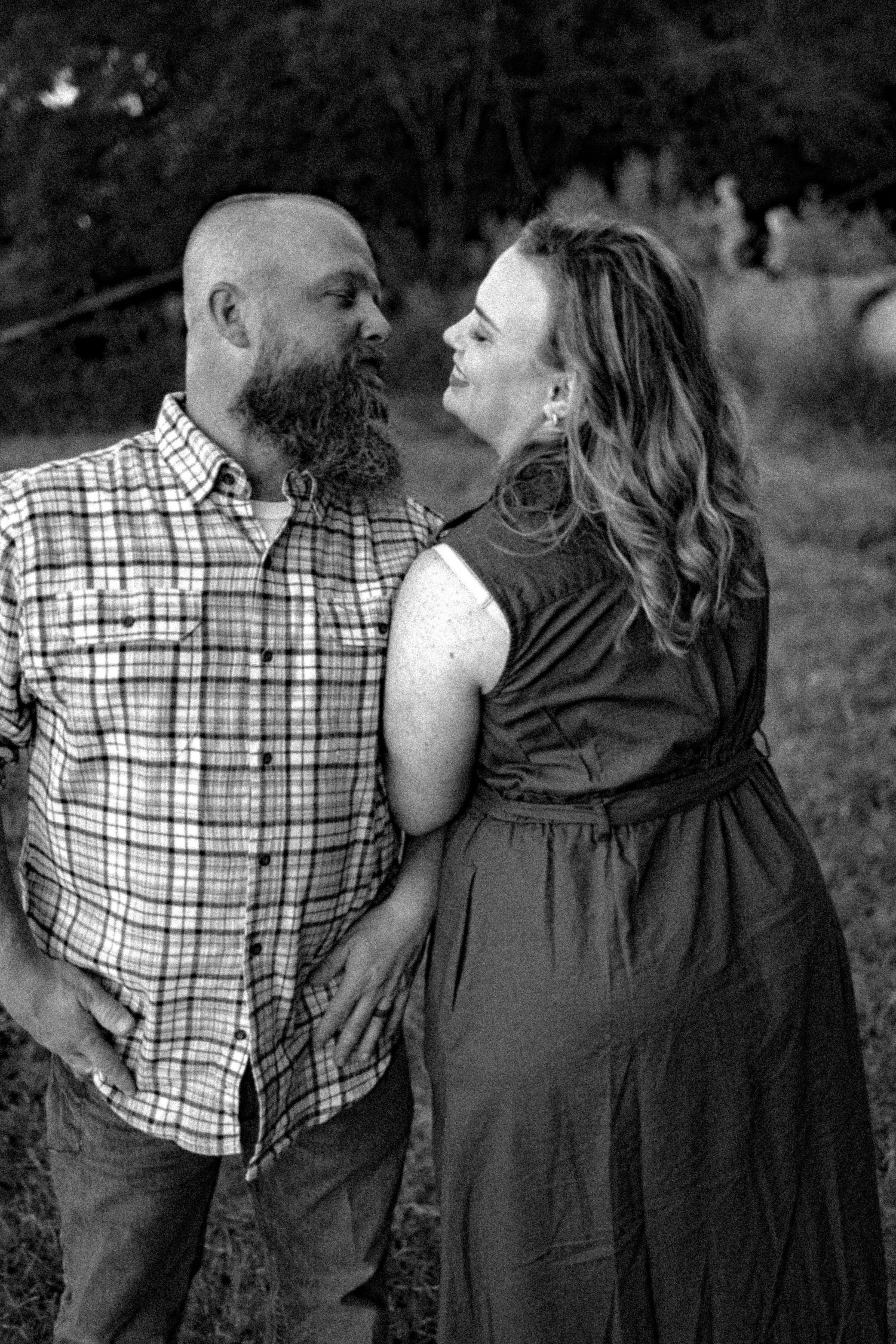 A black and white photo series showing a couple in plaid shirt and dark dress embracing in an outdoor setting.
