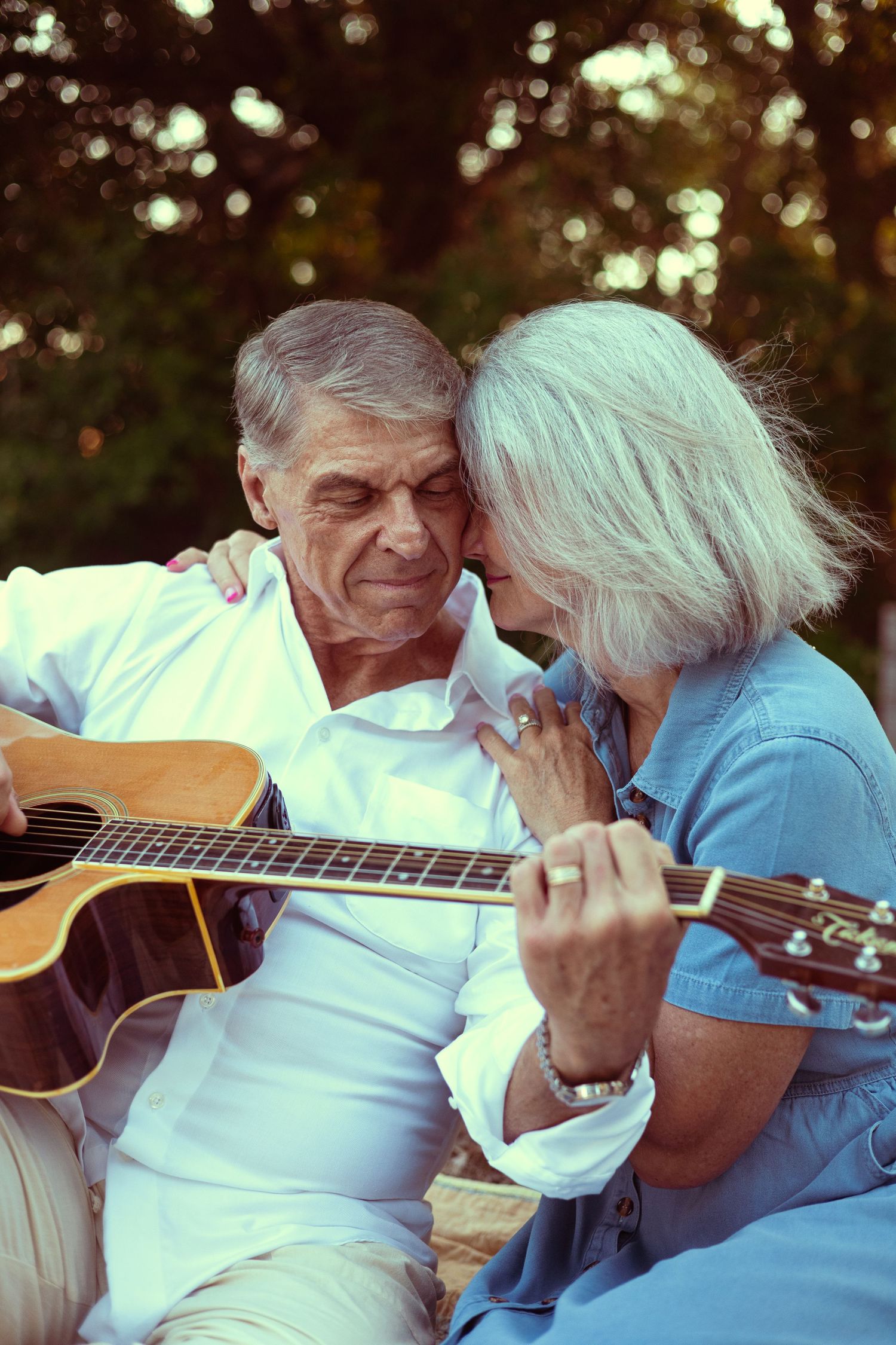 Elderly couple sharing a romantic moment outdoors, man playing acoustic guitar while woman leans in close.