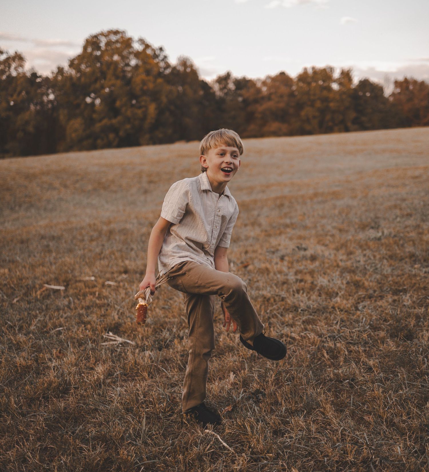 Child playing and running joyfully through a sun-drenched autumn field at dusk.