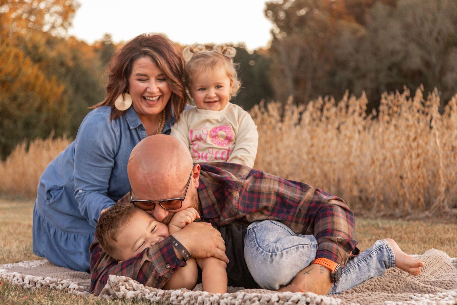 Family lying together in a golden autumn field during sunset photo session.