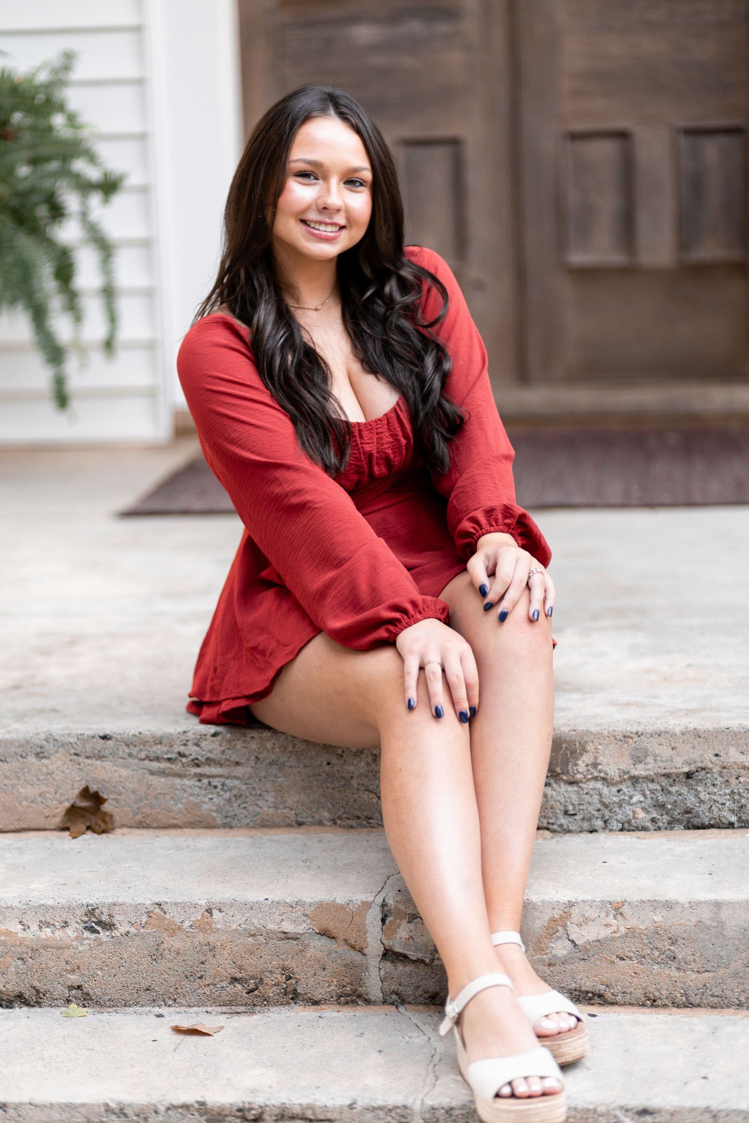 Someone in a red long-sleeved top sits on concrete steps outdoors in a casual pose.