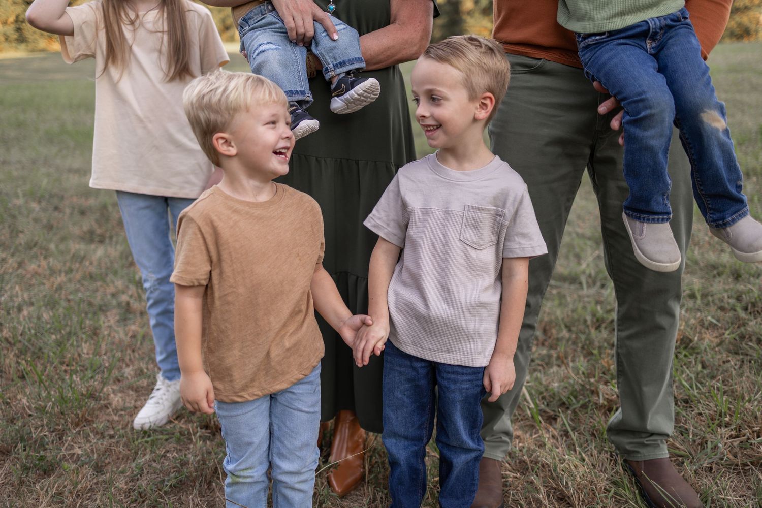 Two young children in casual clothing stand together laughing and smiling on grass.