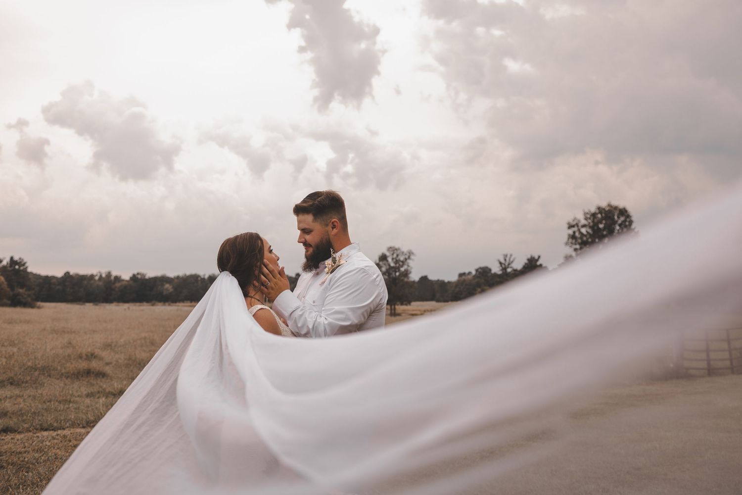 A couple embraces on a misty hillside as a flowing white veil creates a dramatic silhouette against the cloudy sky.