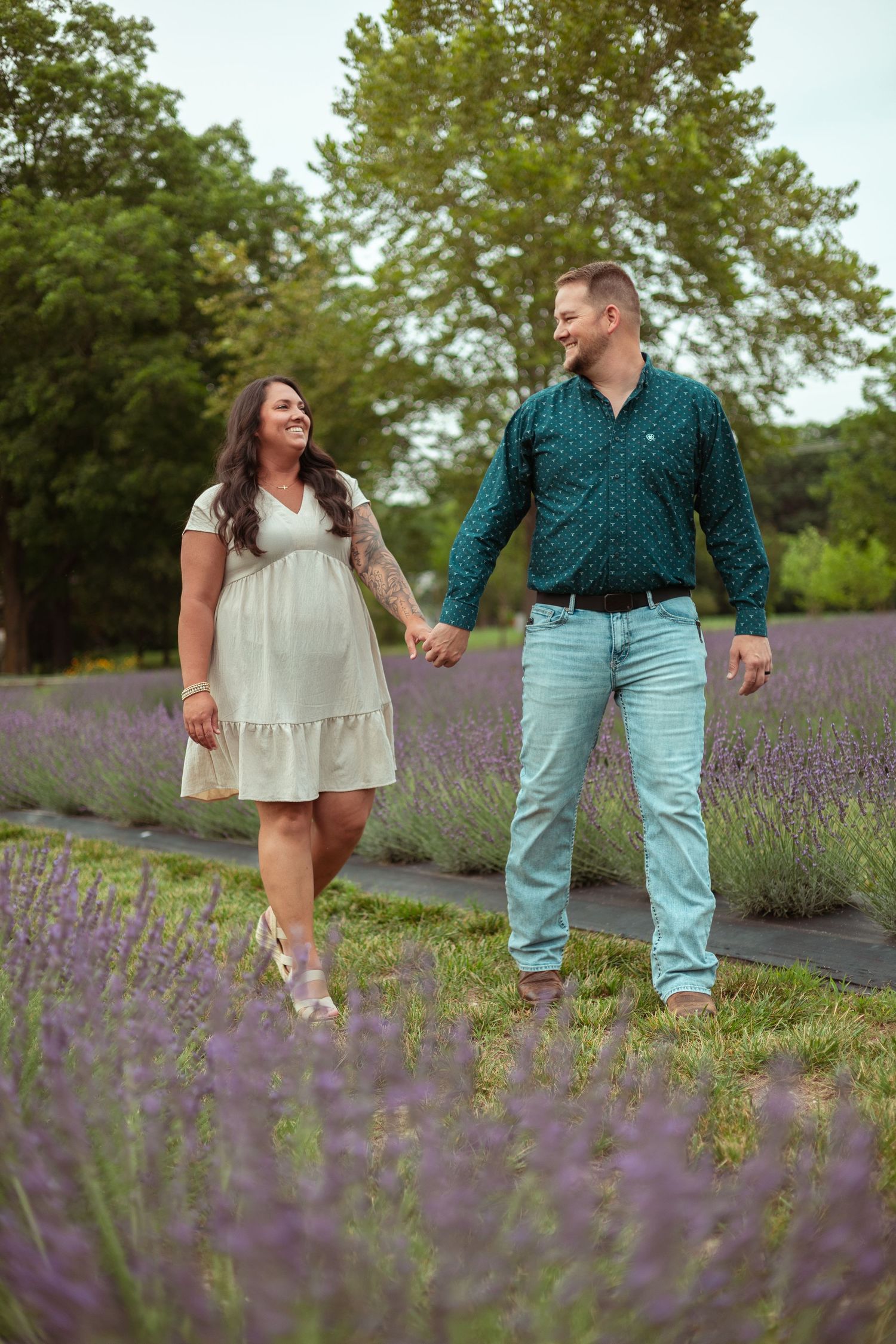 Couple holding hands and smiling while walking through a blooming purple lavender field.