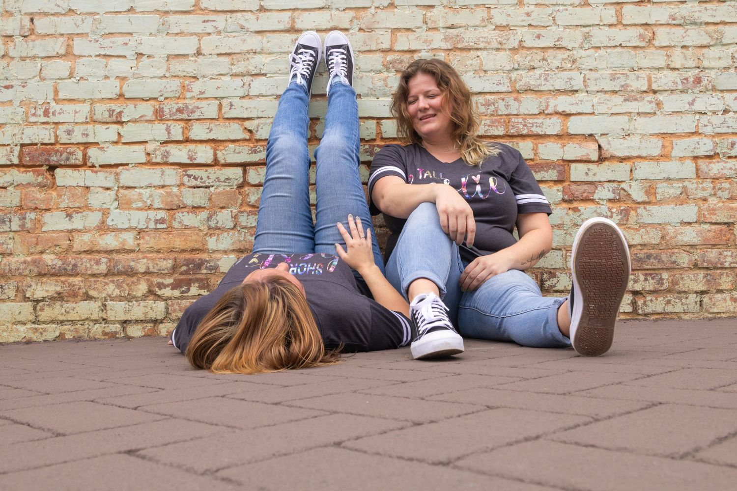 People sitting on a brick wall against a weathered brick background enjoying a casual moment.