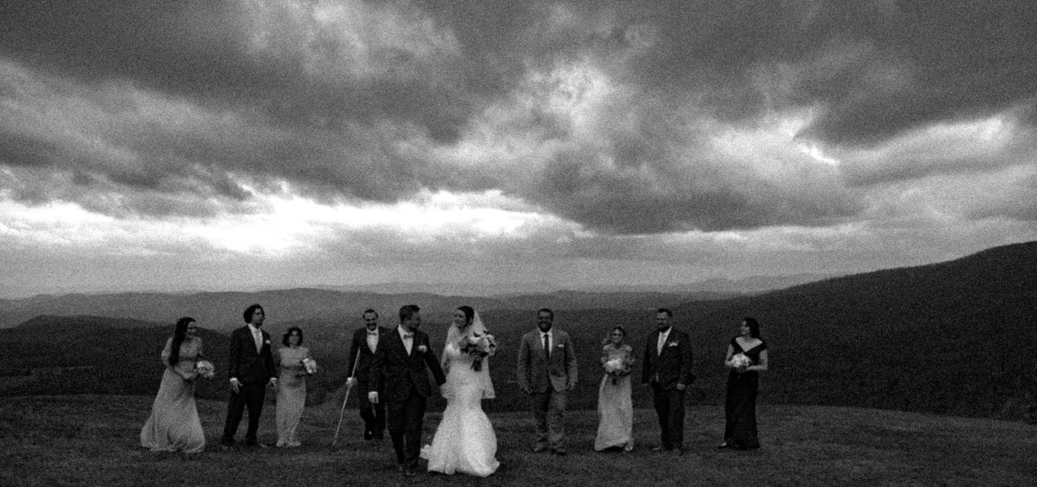 Wedding party lined up on mountaintop under dramatic storm clouds in black and white photography.