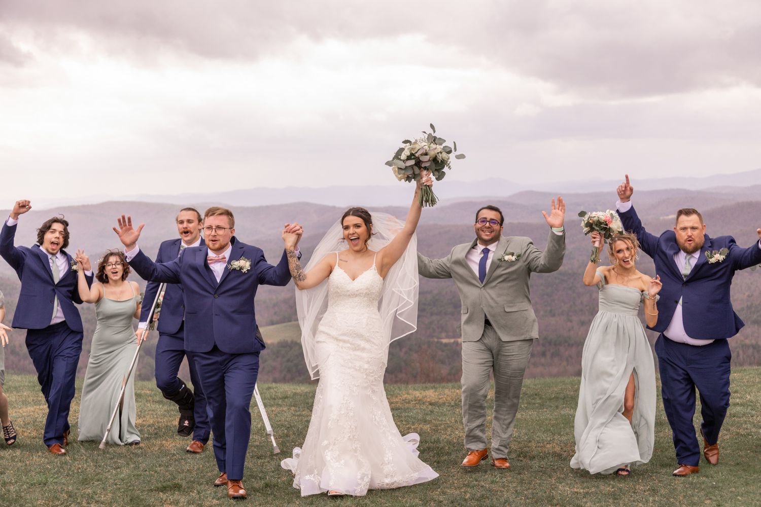 Wedding party celebrates with raised arms against a mountain landscape background.