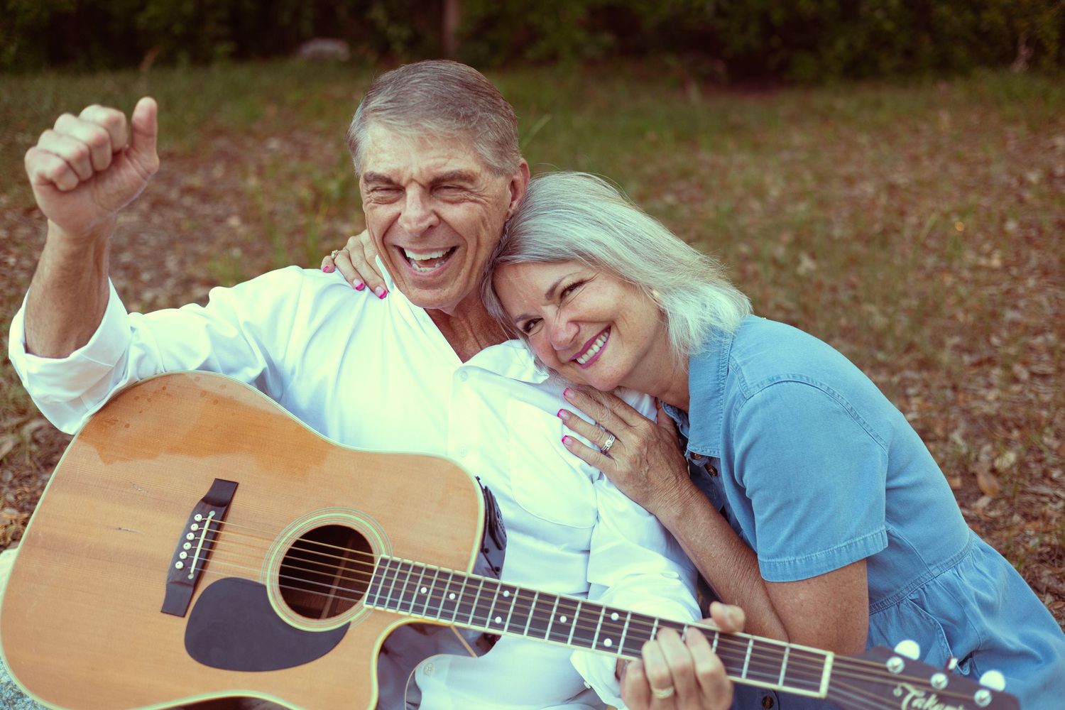 Happy senior couple sitting outdoors with acoustic guitar, smiling and enjoying music together in a park setting.