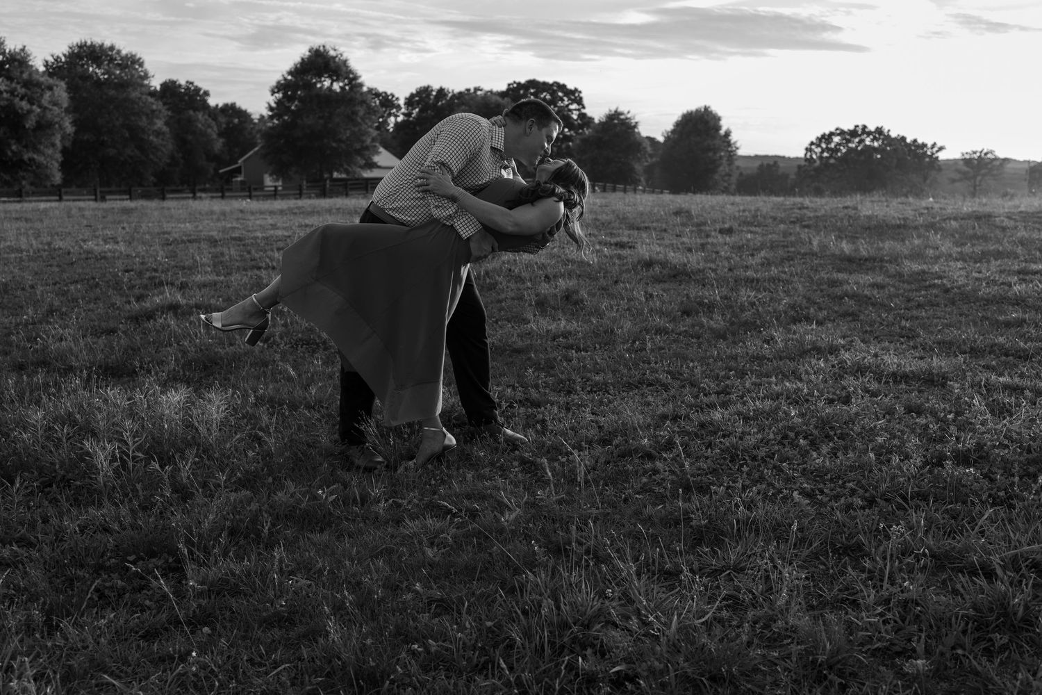 Black and white photo of a couple dancing romantically in an open field at dusk.