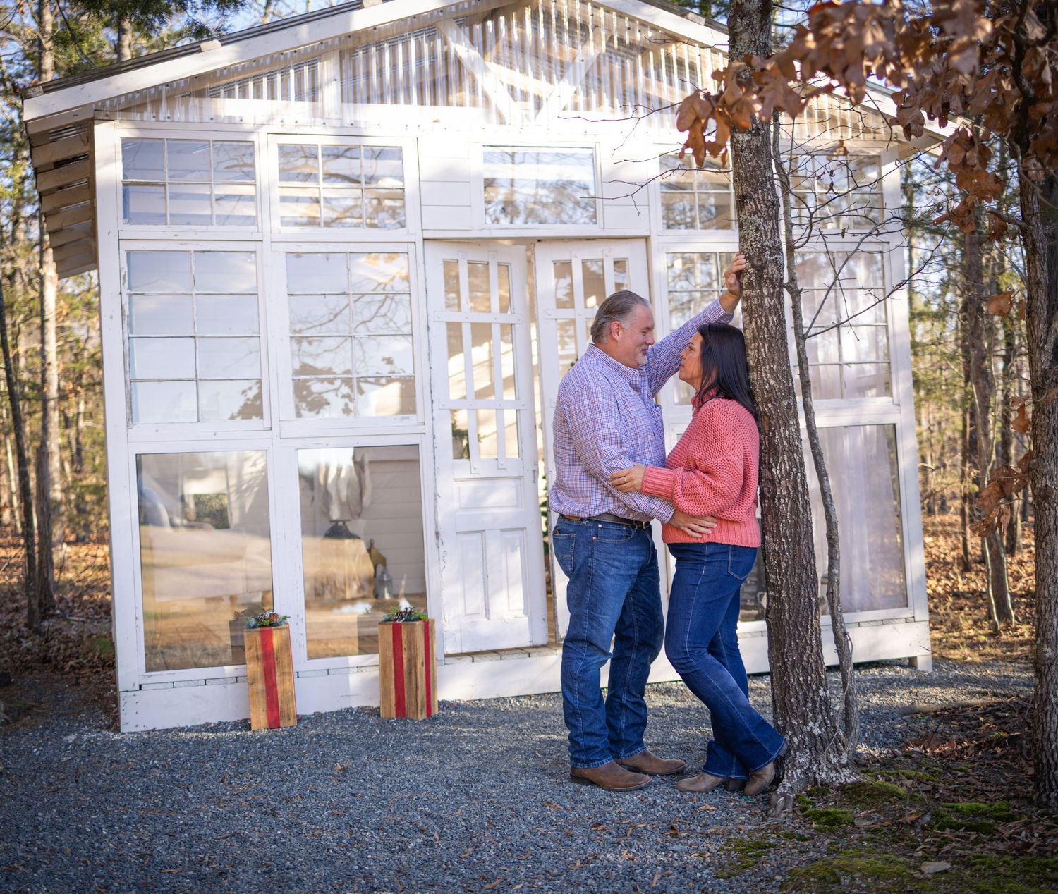 A couple stands together in front of a white gazebo structure surrounded by autumn trees in a park setting.