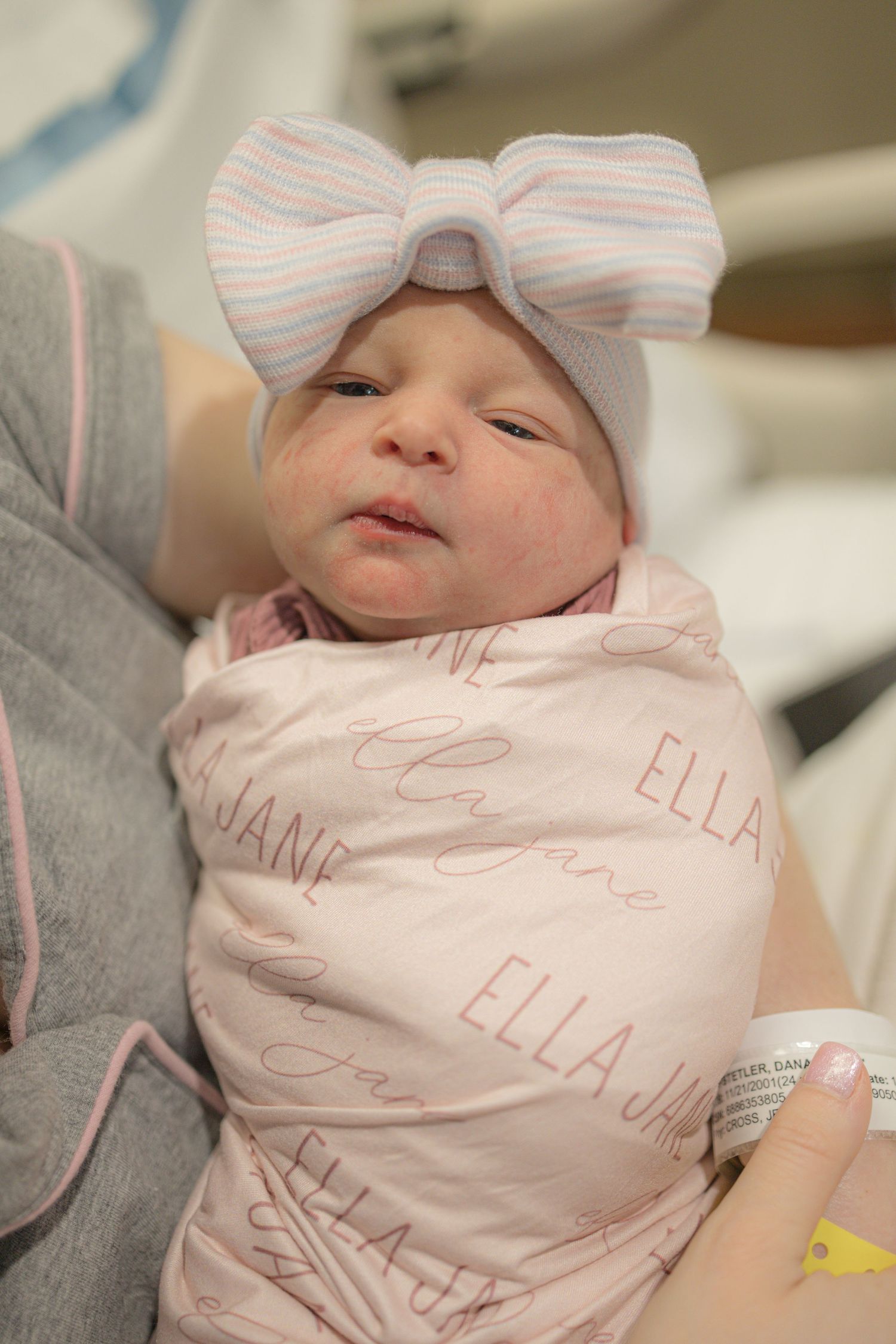 A newborn baby wrapped in a pink striped blanket with their name embroidered on it.