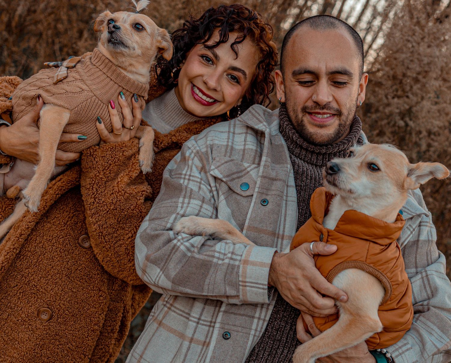 A couple in winter coats share joyful moments together while sitting outdoors in an autumn setting.