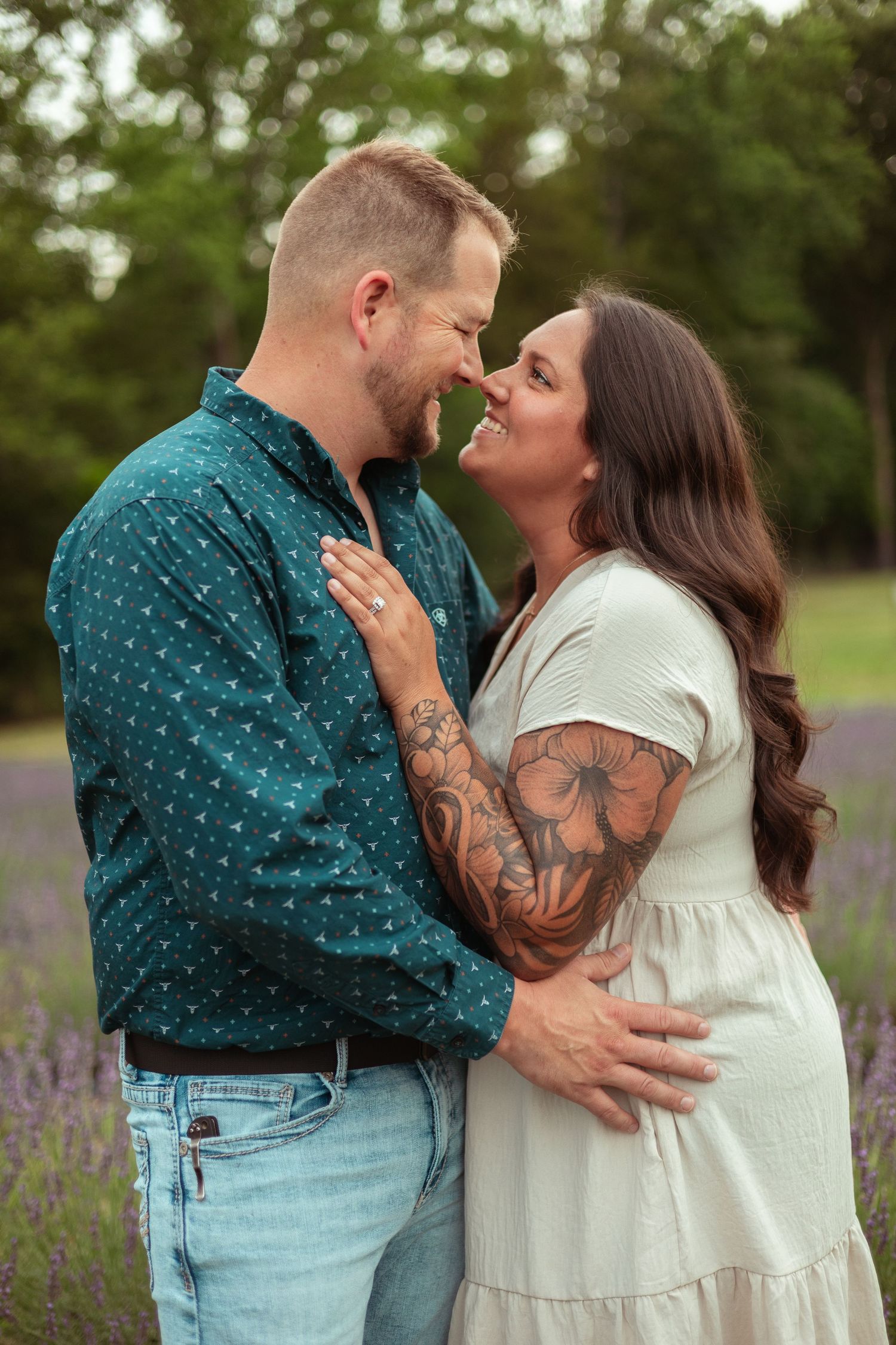A couple shares a romantic moment in a lavender field, the woman\u2019s tattooed arm resting on her partner\u2019s chest.