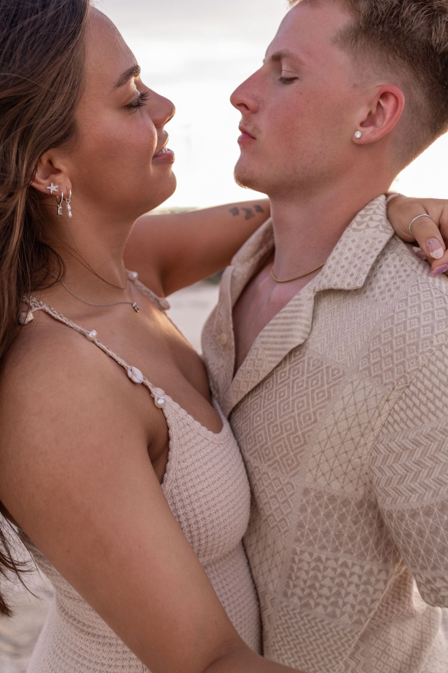 Romantic couple in matching beige outfits embrace in intimate moment at sunset.