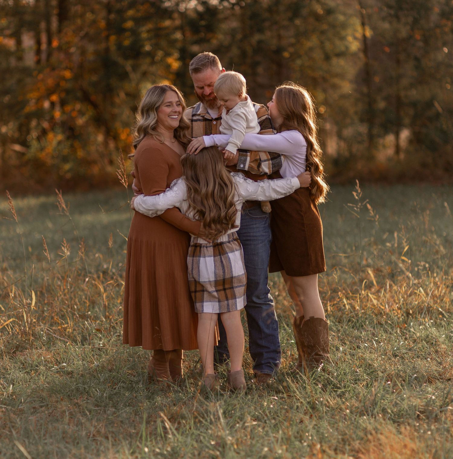 Family embracing together in a golden autumn field at sunset with warm glowing light.