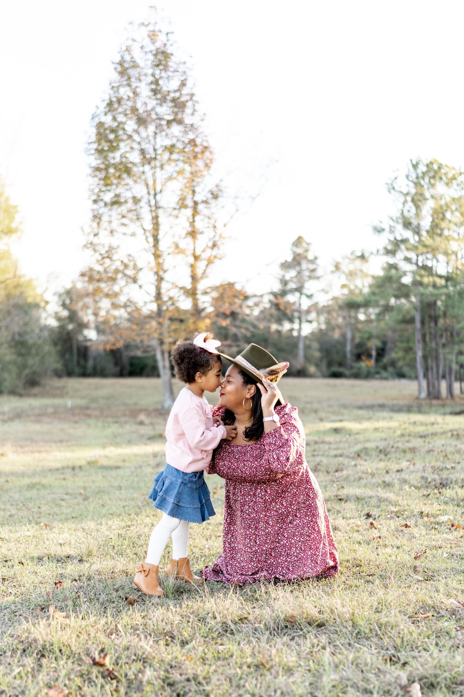 Two people share a tender moment sitting together in a sunlit grassy field during golden hour.