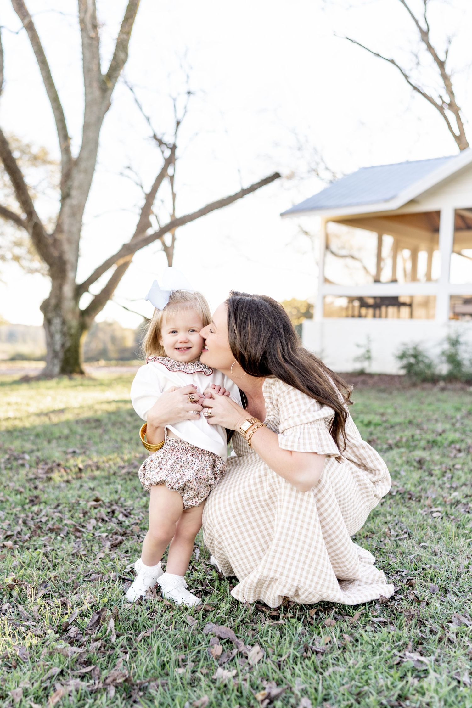 A tender outdoor moment between parent and child wearing matching neutral dresses in a rustic backyard setting.
