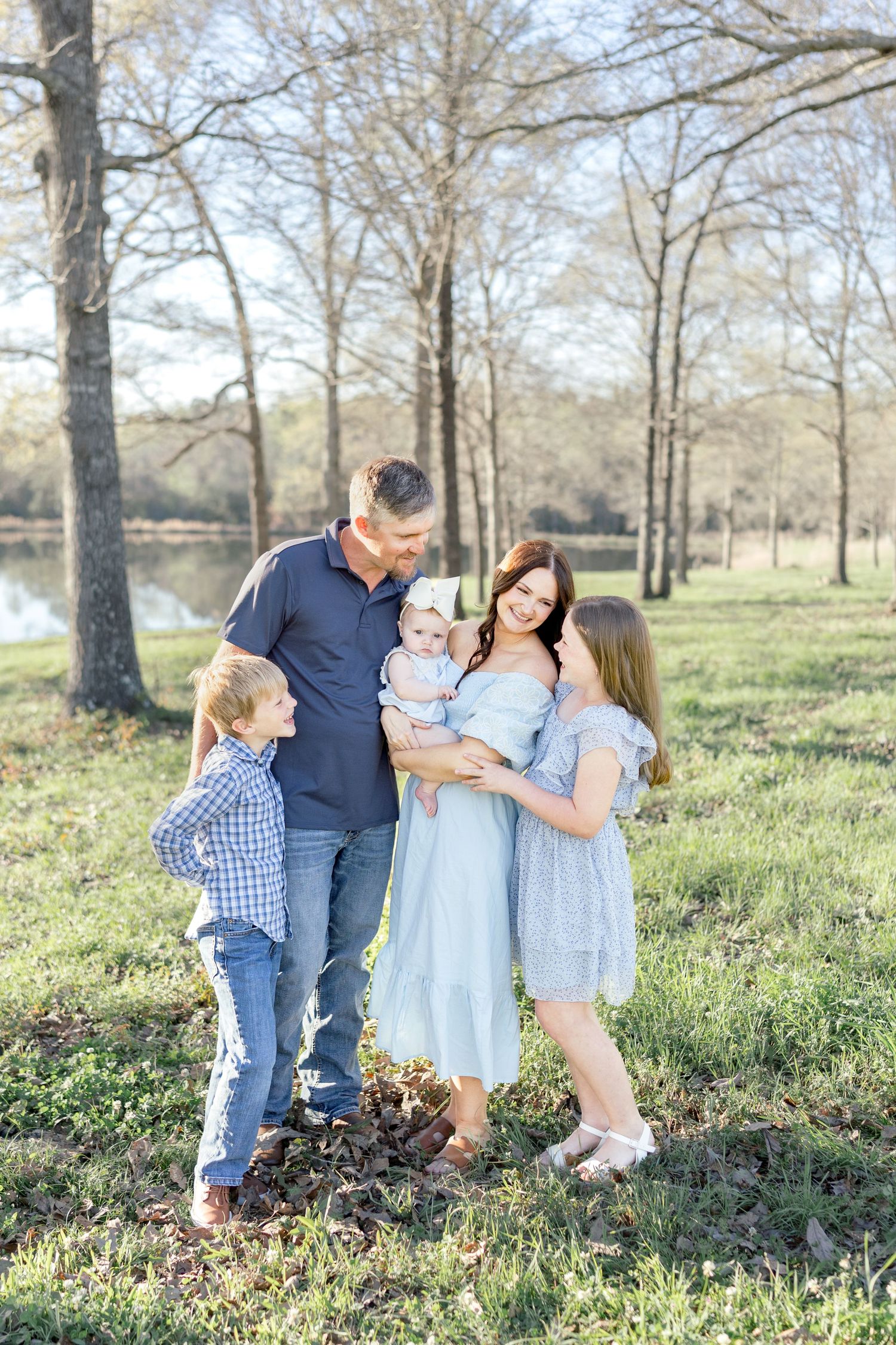A family shares joyful moments together in a sun-dappled wooded area during a spring outdoor photo session.