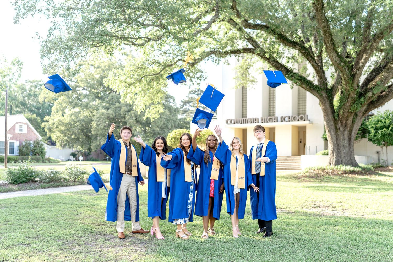 Graduates in blue caps and gowns toss their mortarboards into the air during an outdoor graduation celebration located in Columbia, MS