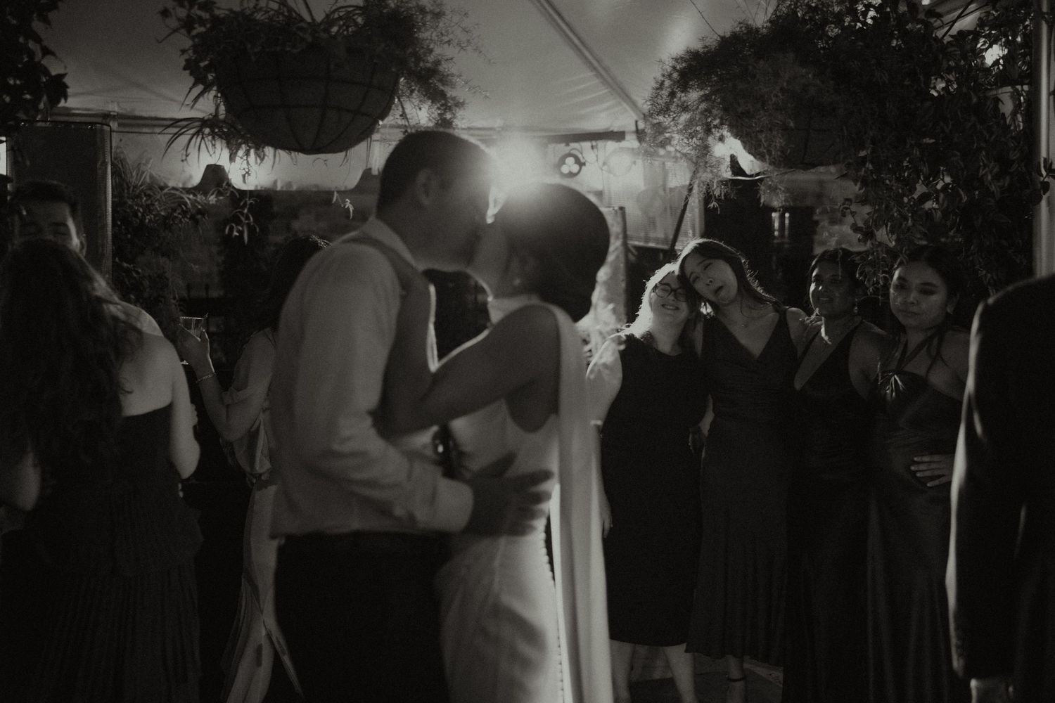 Black and white photo of a couple sharing their first dance kiss at a wedding reception under a tent.