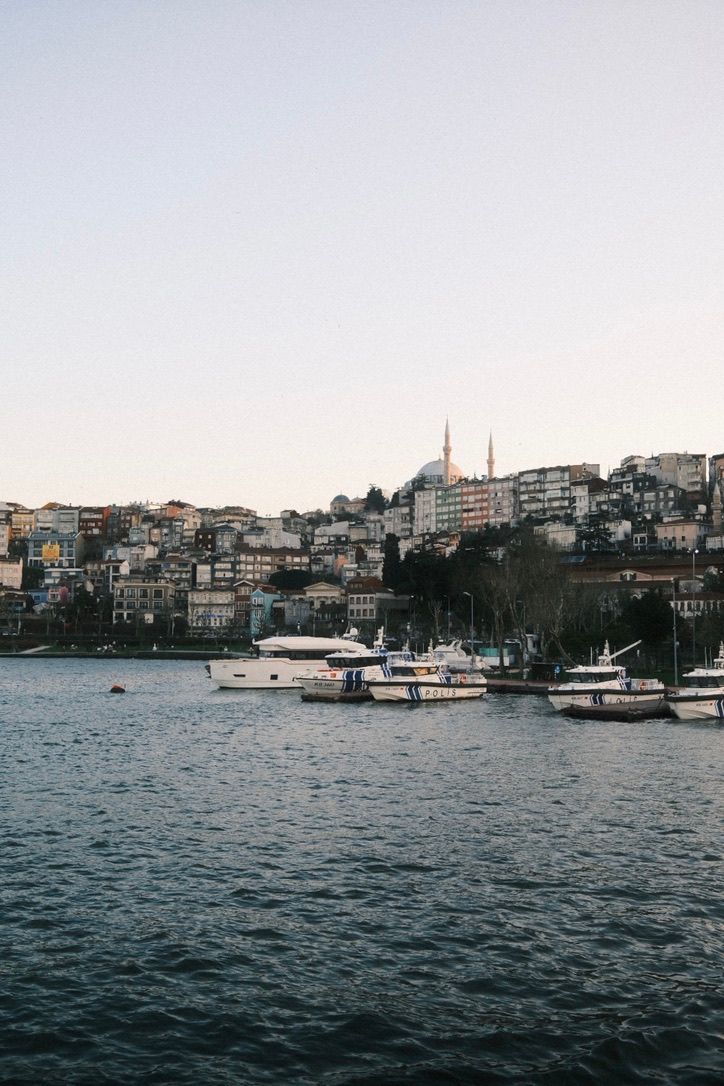 Istanbul waterfront skyline with boats docked on the Bosphorus, historic mosque minarets rising above densely packed hillside buildings.