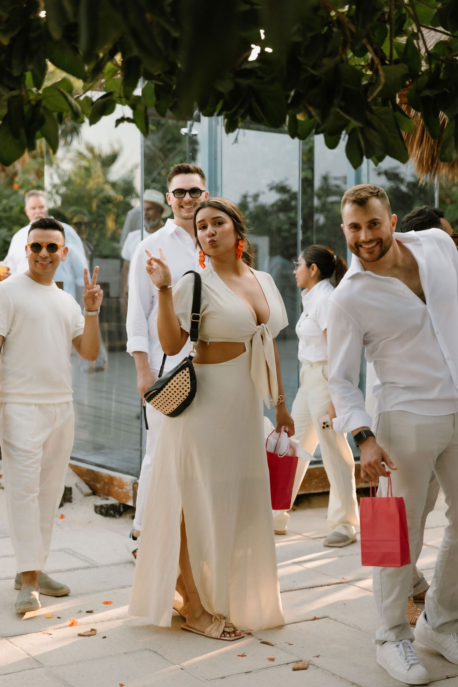 Group of friends dressed in white outfits posing outdoors at a stylish event, woman in center wearing elegant cream dress.