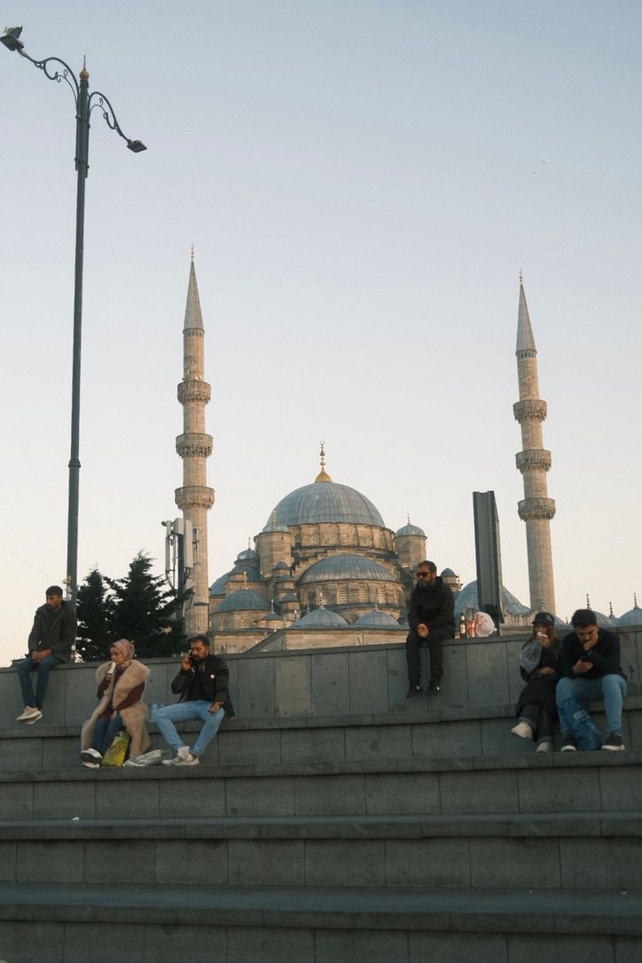 People sitting on steps with the iconic Blue Mosque featuring twin minarets and large domes in Istanbul, Turkey.