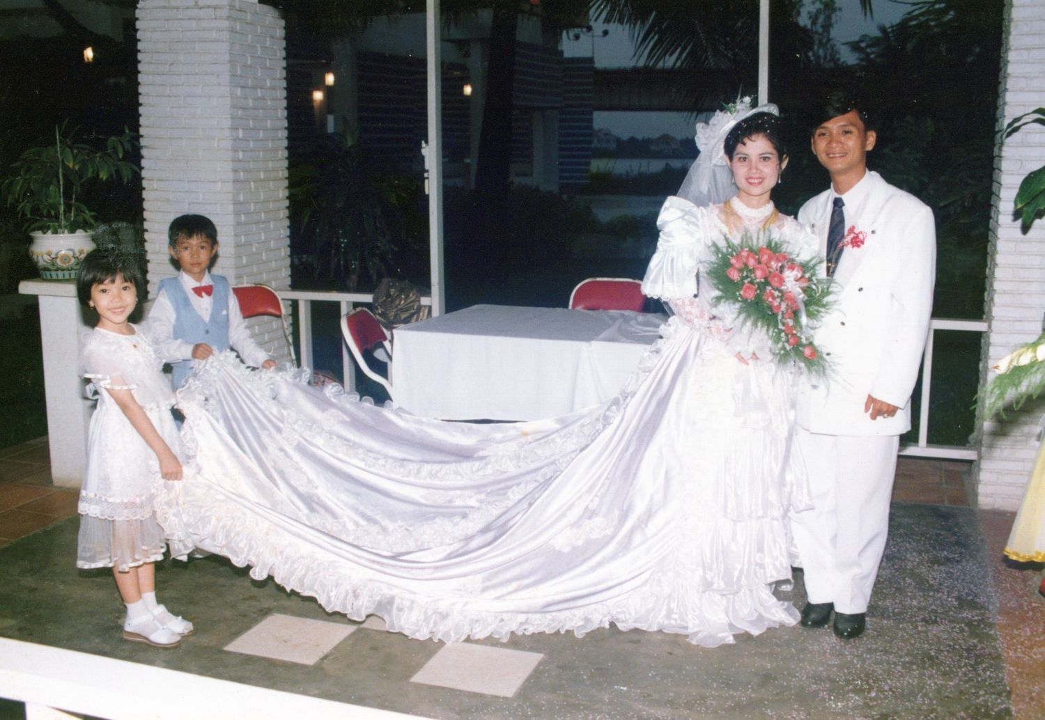 Bride and groom pose with two children at a wedding, bride wearing a long white gown with an elegant train.