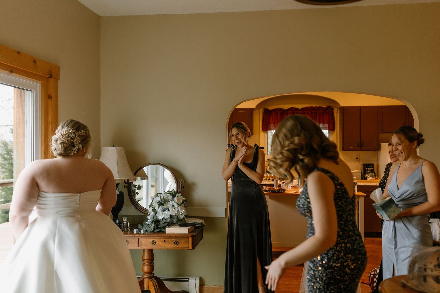 Bride in white wedding gown with bridesmaids getting ready in rustic room before wedding ceremony.