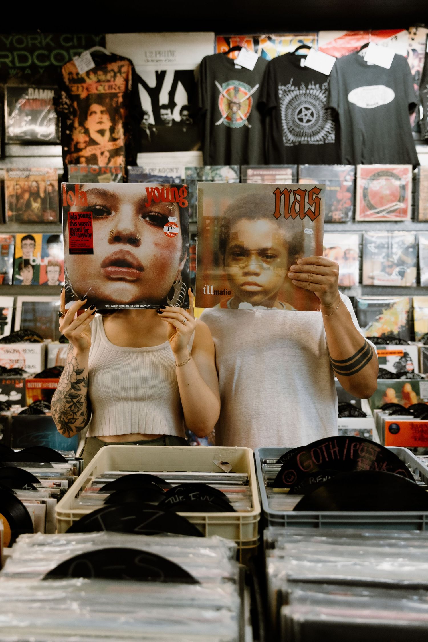 Tattooed person holding Nas and Yung Lean vinyl records in a music store filled with albums and band tees.