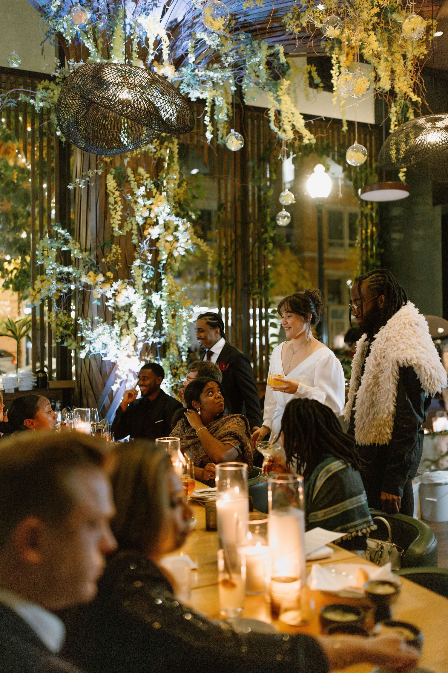 Elegant indoor wedding reception with floral ceiling decor, candlelit tables, and guests mingling in a warmly lit venue.