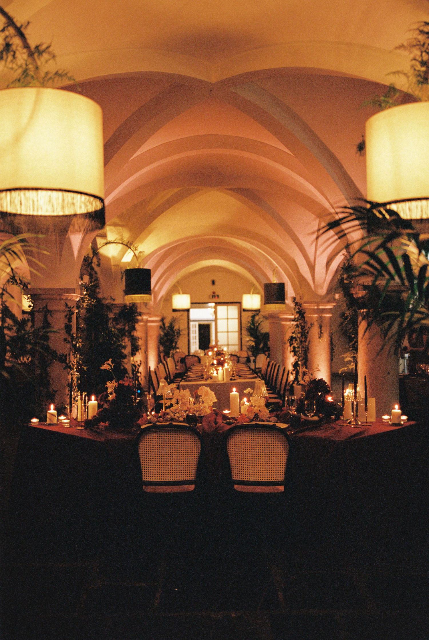 Elegant candlelit dining hall with vaulted ceilings, lush greenery, and warm ambient lighting for a formal event.