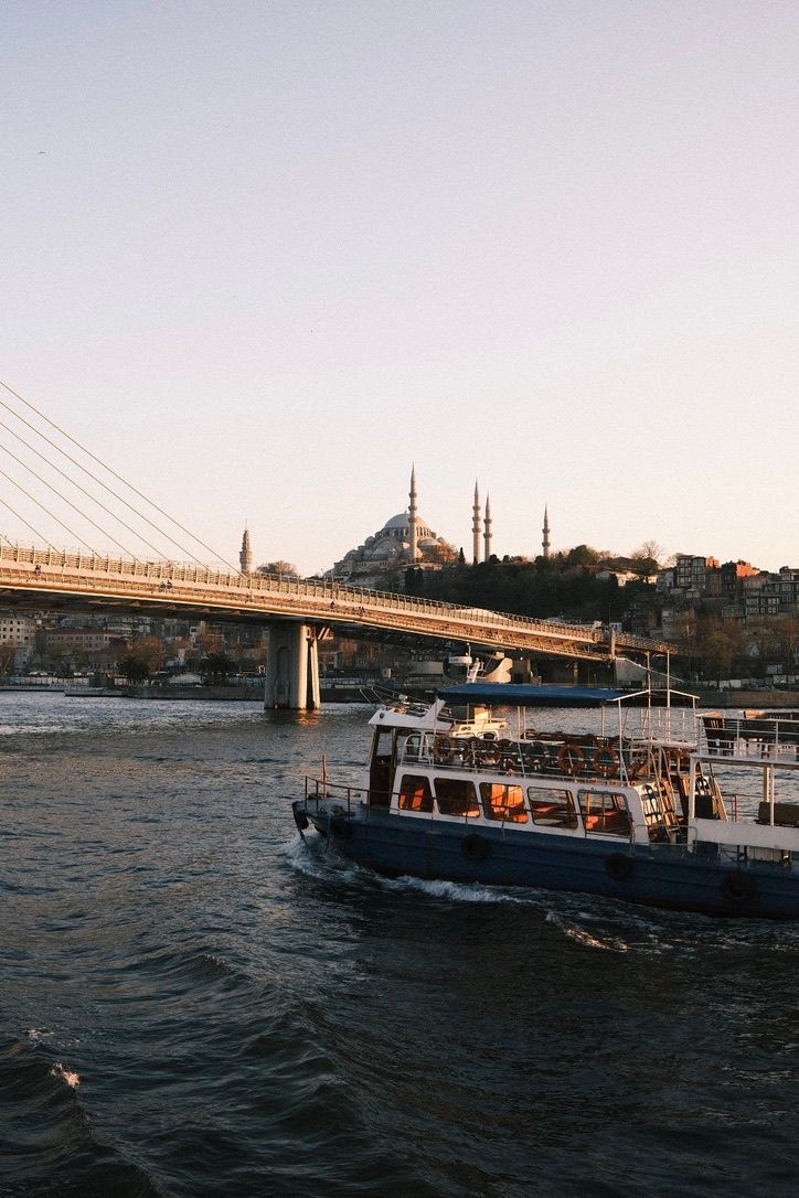 A ferry boat cruises the Bosphorus Strait with the Suleymaniye Mosque and Golden Horn Bridge in Istanbul, Turkey at sunset.